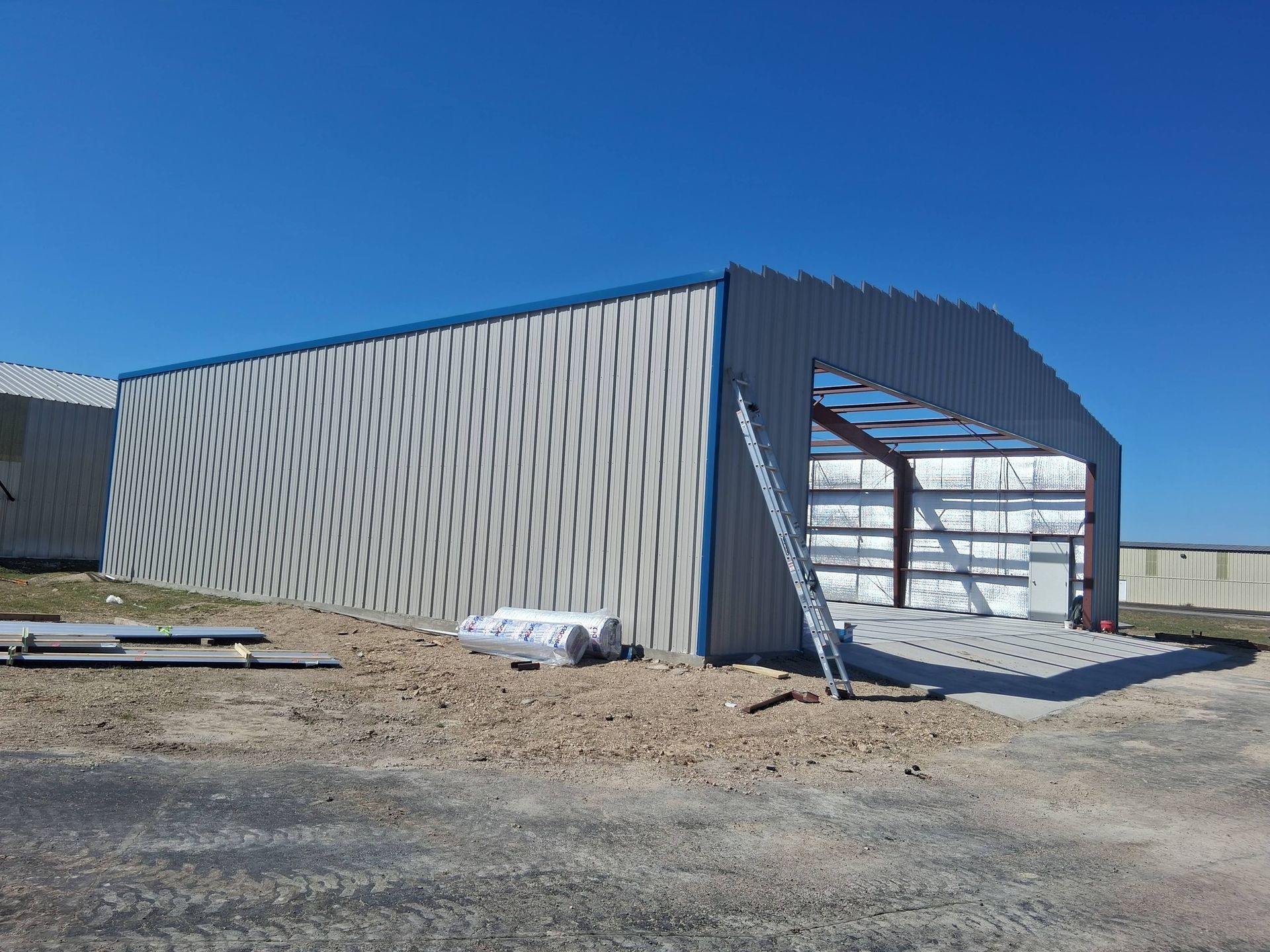 Industrial building under construction with corrugated metal walls and open front framing.