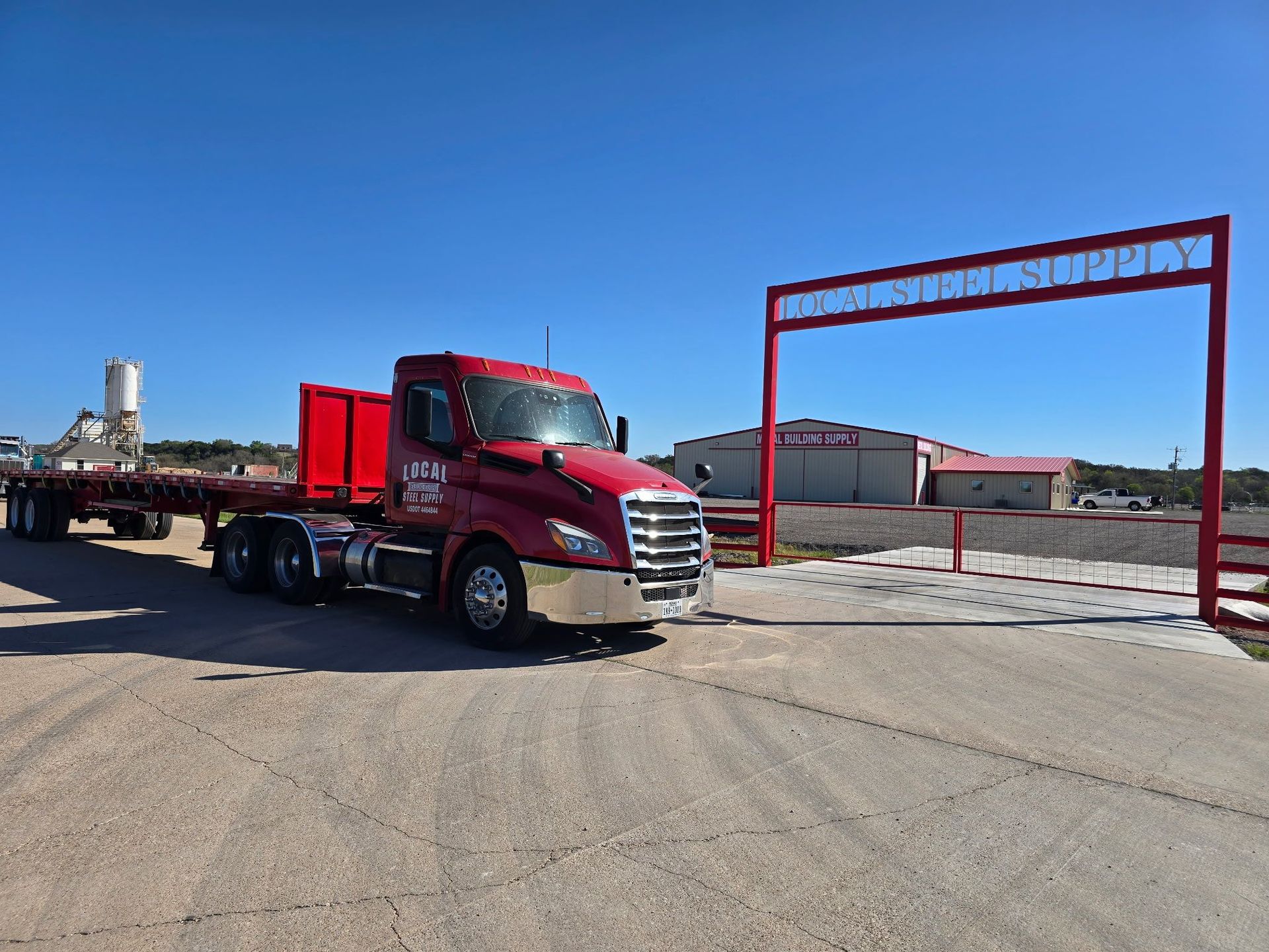 Red semi truck parked by a red gate in an industrial lot under a clear blue sky