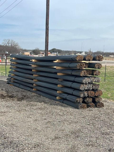 Stacked black metal fence panels on gravel in an outdoor yard, with a utility pole and sky in the background