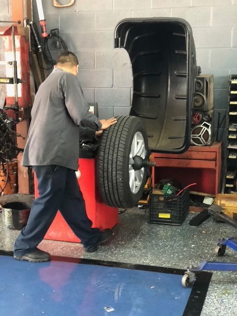 Mechanic lifting a wheel near a red tire machine in an auto shop | Rapid Repair Auto Center