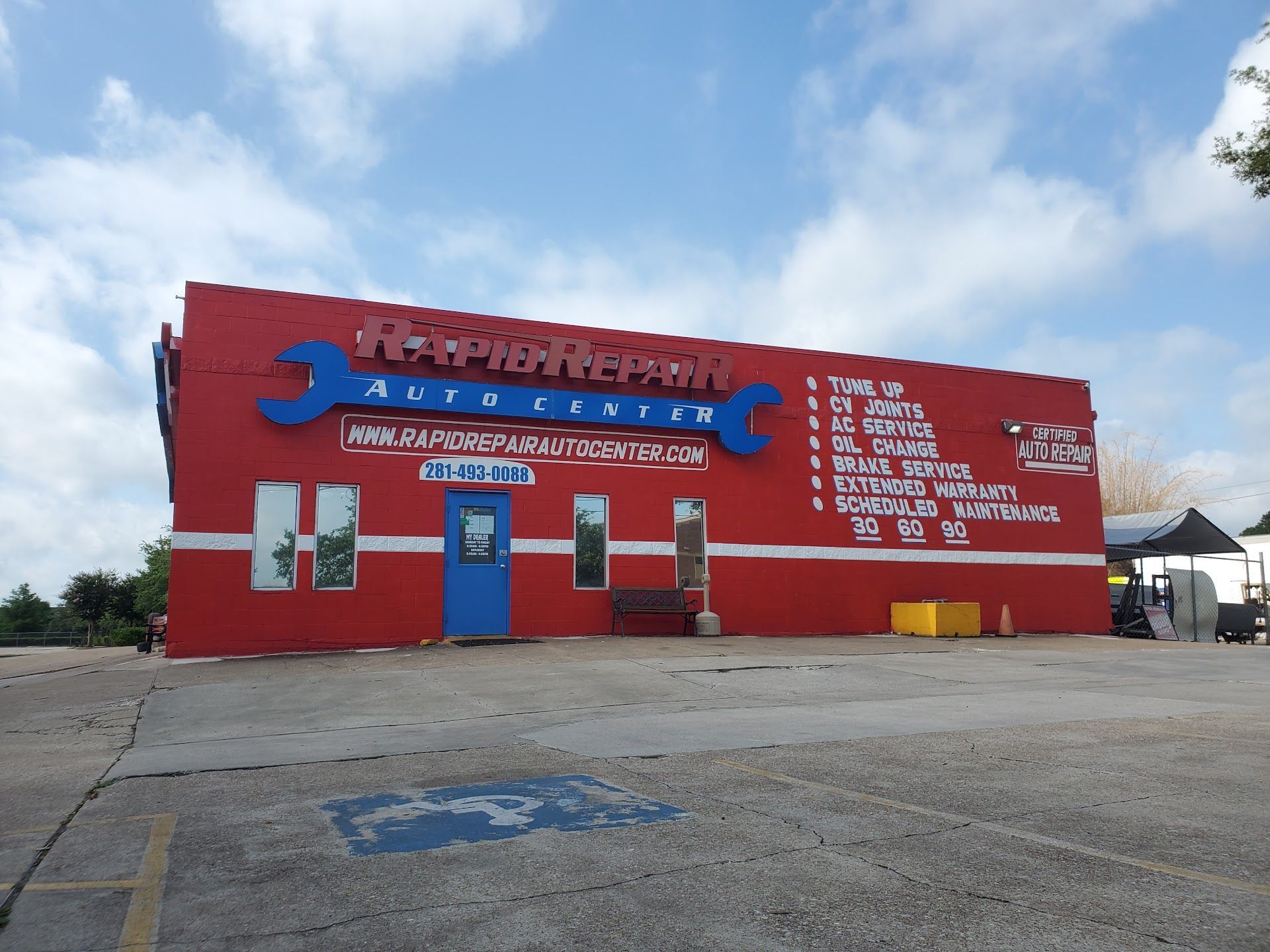 Red auto repair shop with large tools sign on a sunny day, parked cars nearby | Rapid Repair Auto Center