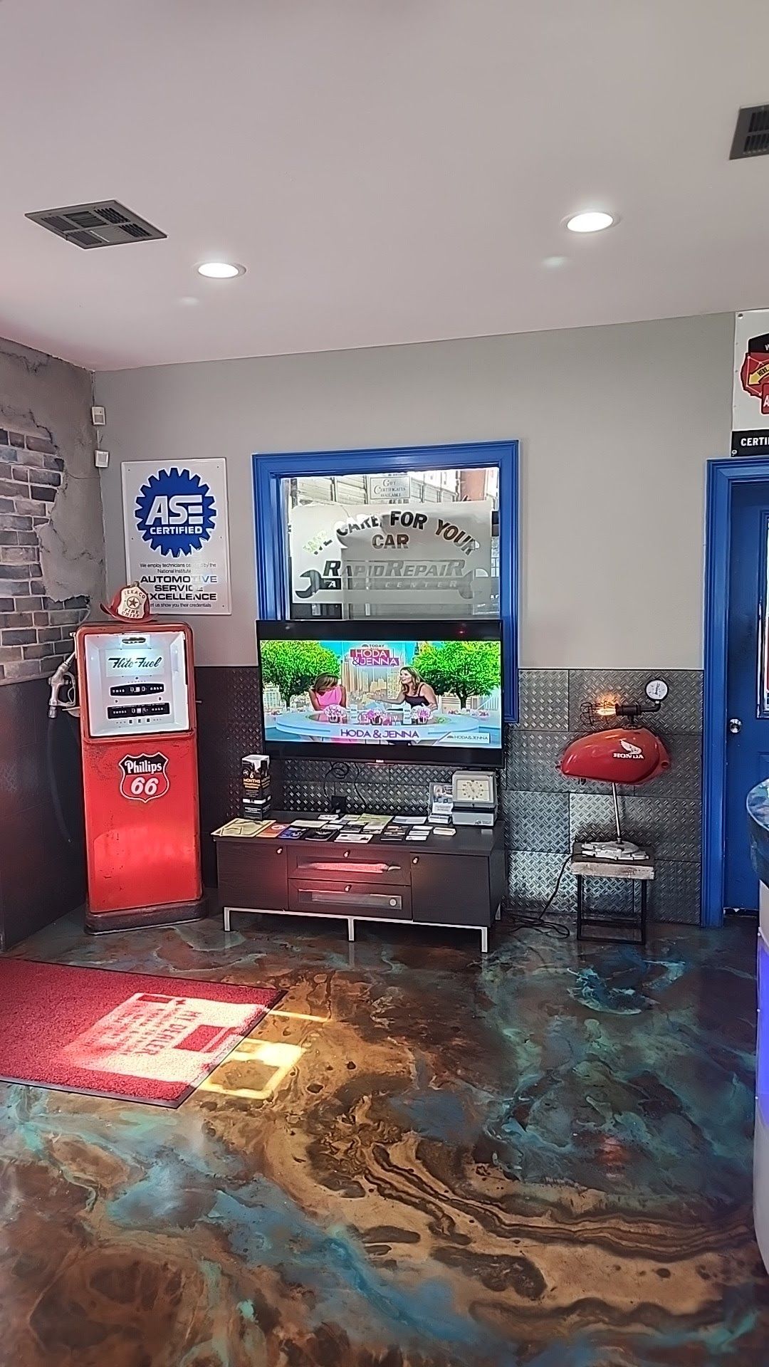 Lobby with a red kiosk, wall-mounted TV, and red stools on a patterned floor. | Rapid Repair Auto Center