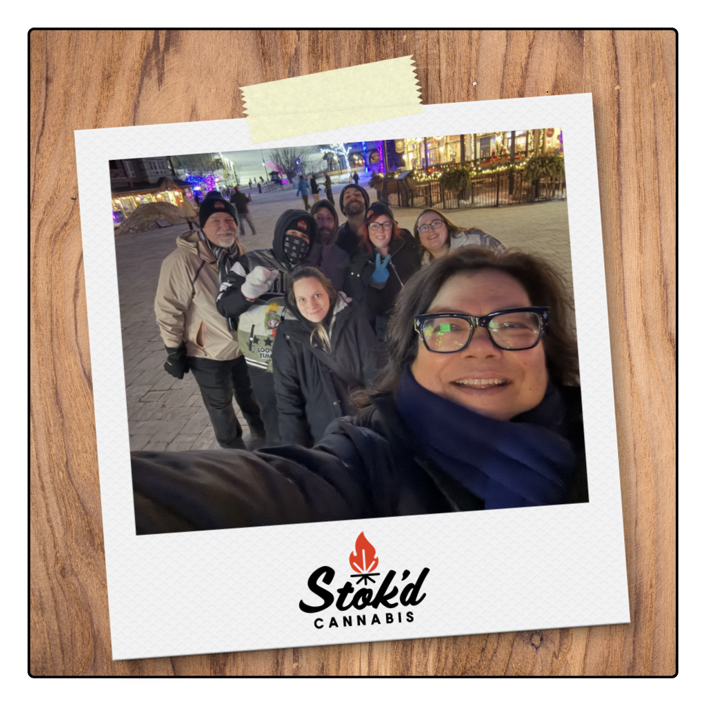 Group selfie outdoors at night, smiling by a taped Polaroid-style photo with Stōkt Campwood logo.