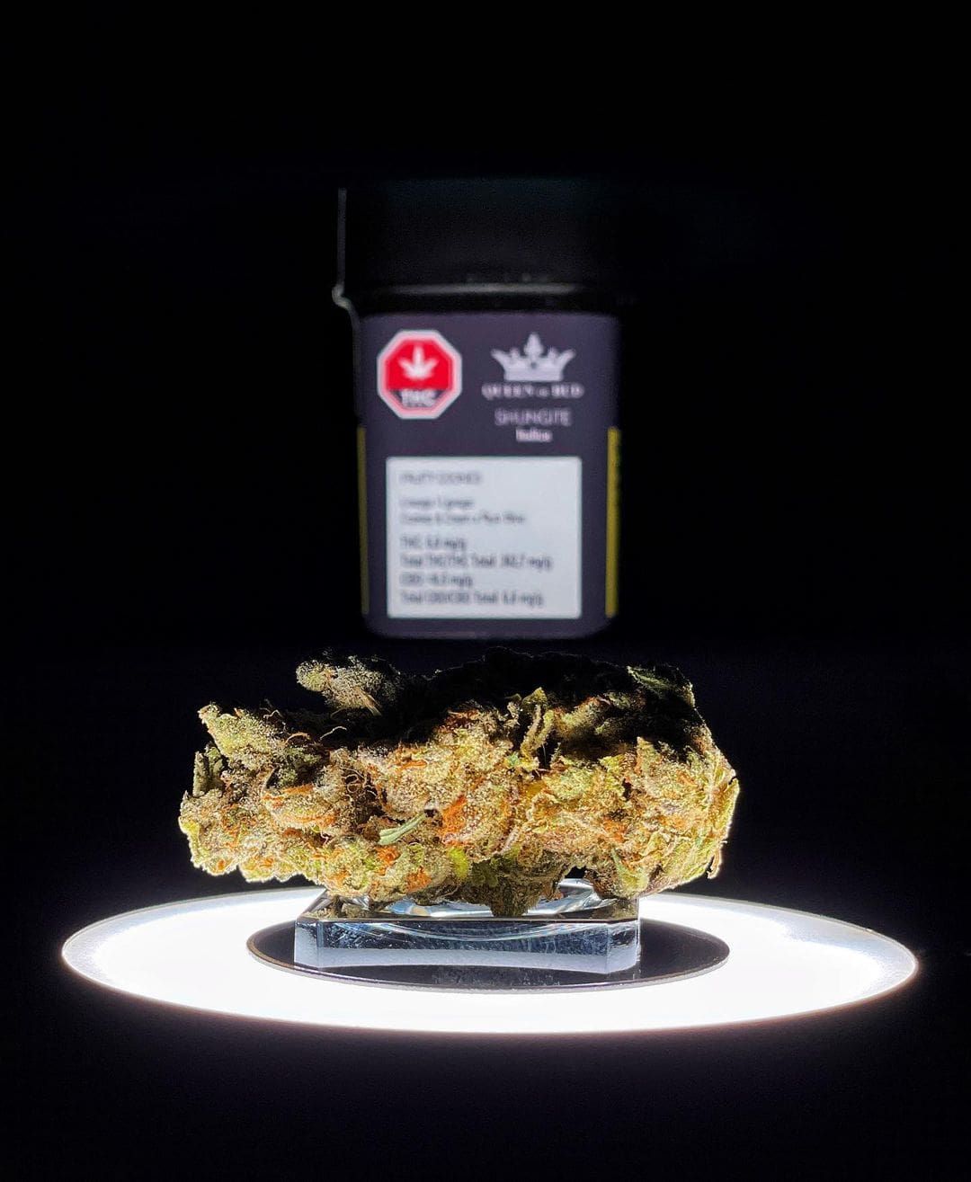 Black cannabis jar above a lit tray with a close-up of a nug against a dark background