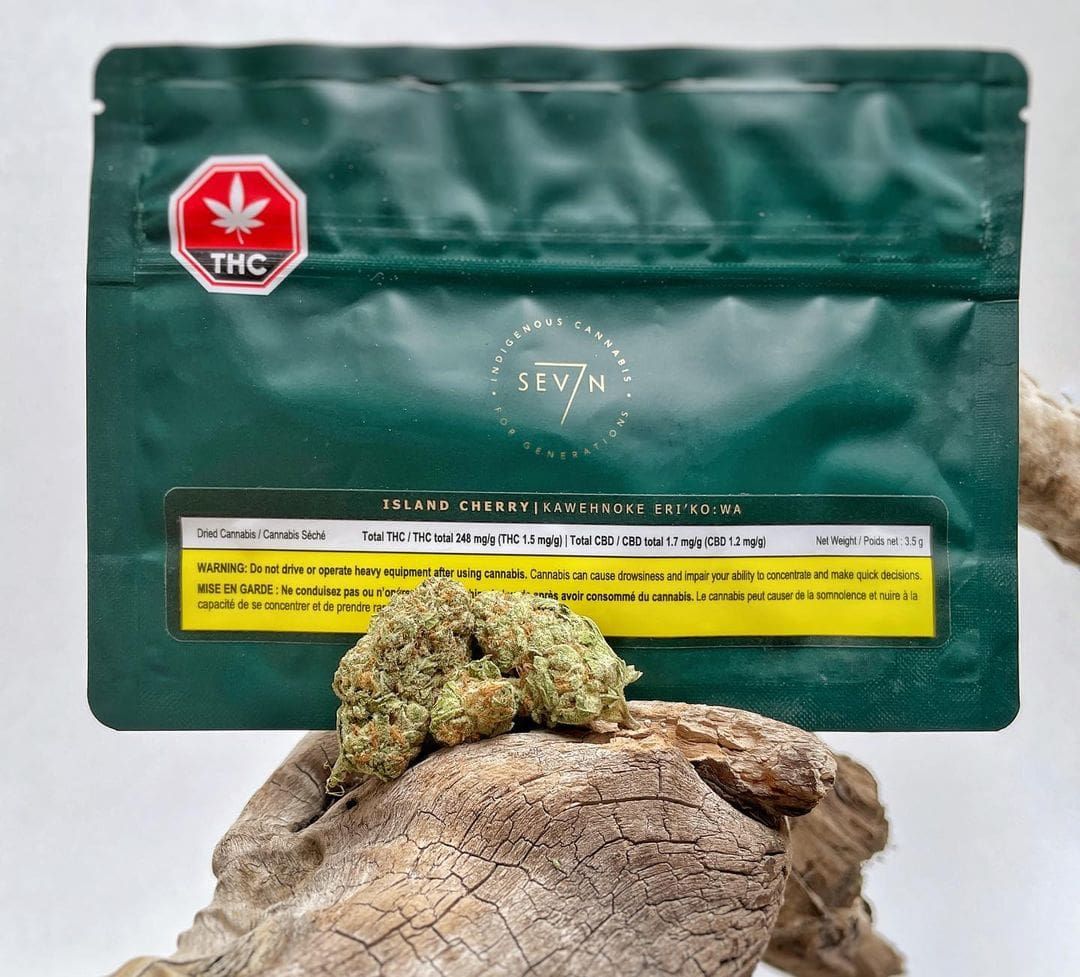 Green cannabis pouch behind a small bud resting on wood, with a red THC maple leaf label
