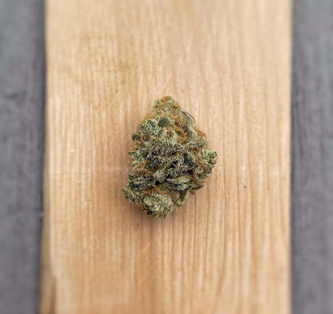 Small green-brown cannabis bud on a light wood surface
