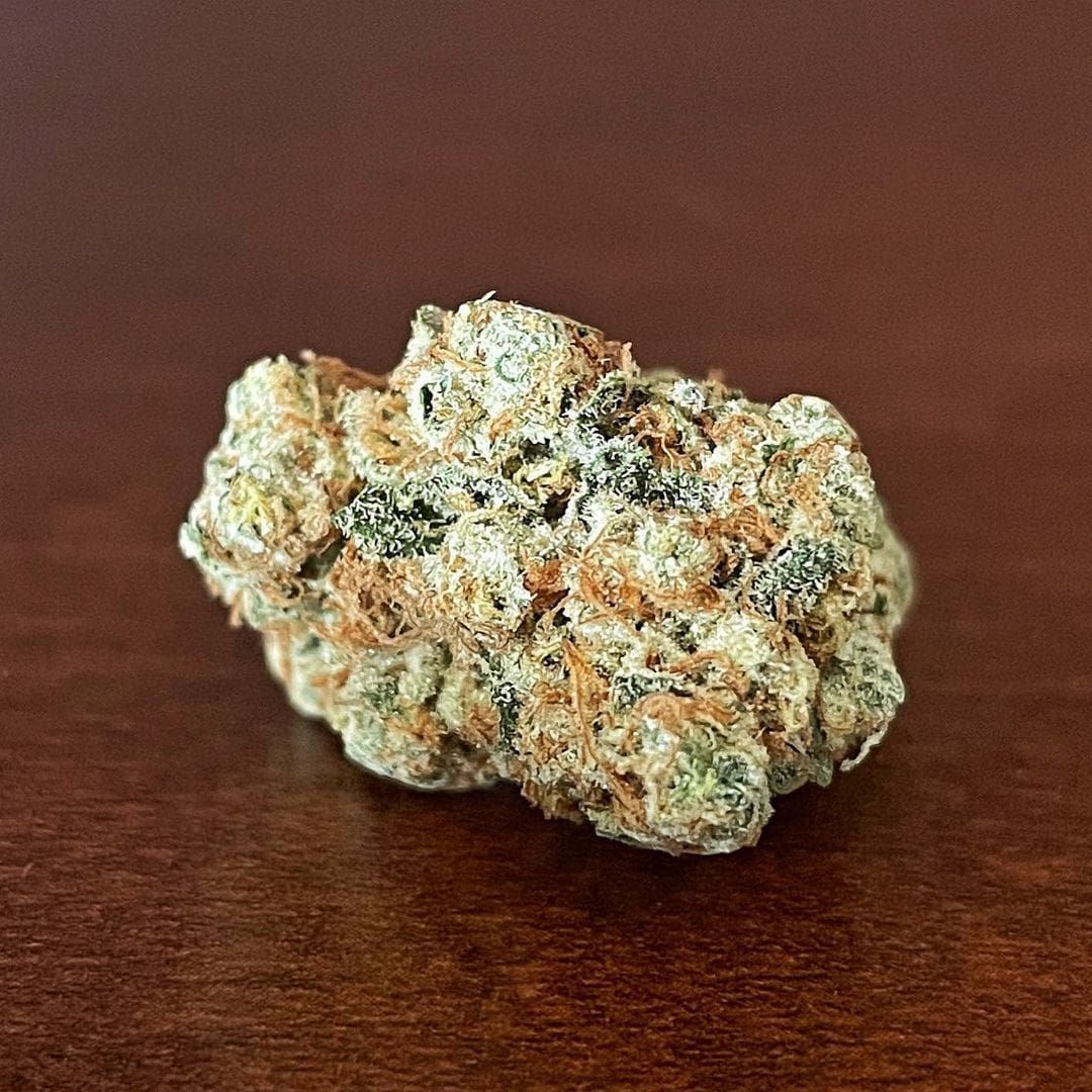 A frosty cannabis bud on a dark wooden surface