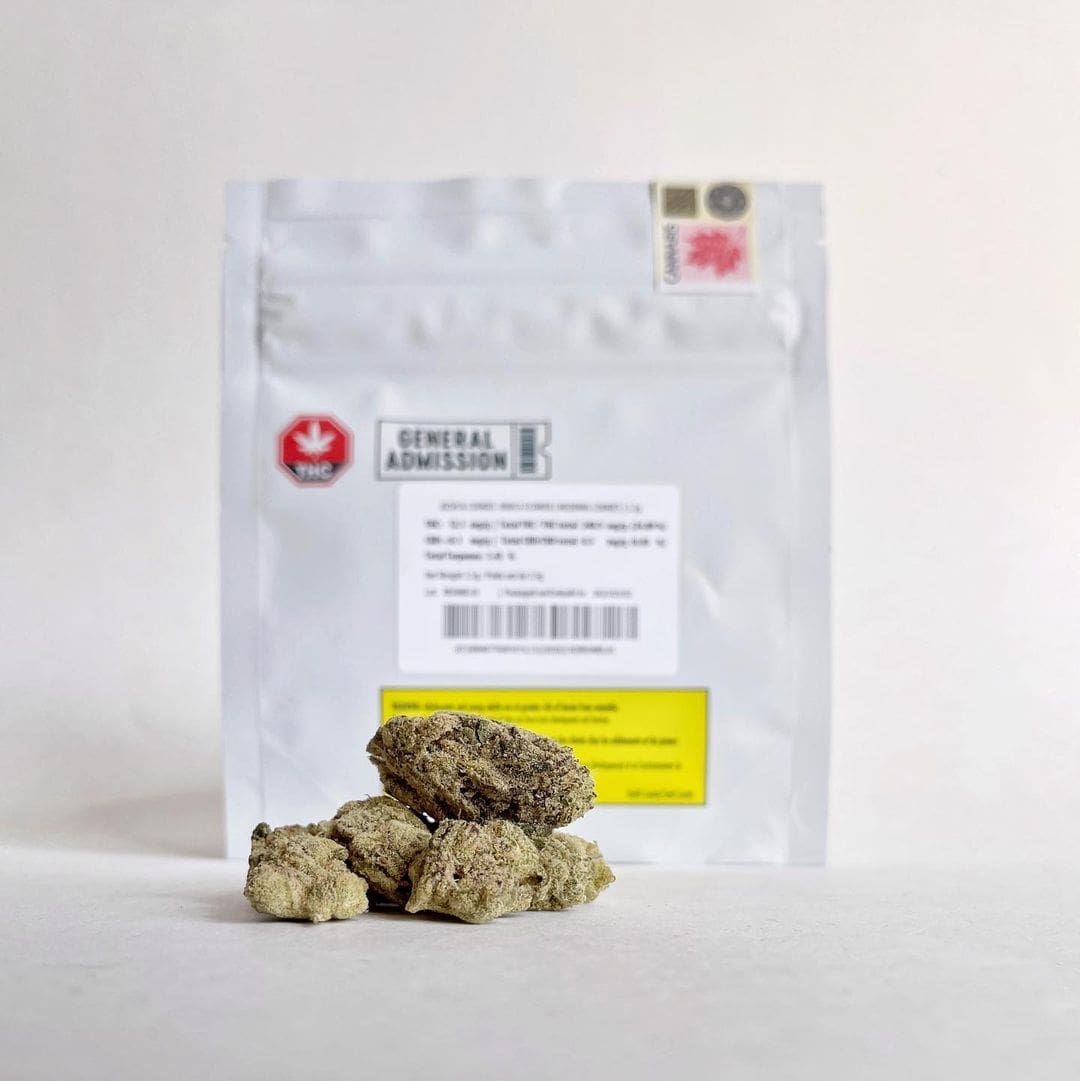White pouch with label behind small beige rocks on a white surface.