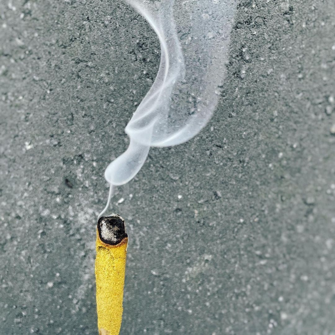 A yellow cigarette butt smoldering on gray pavement with a thin wisp of smoke