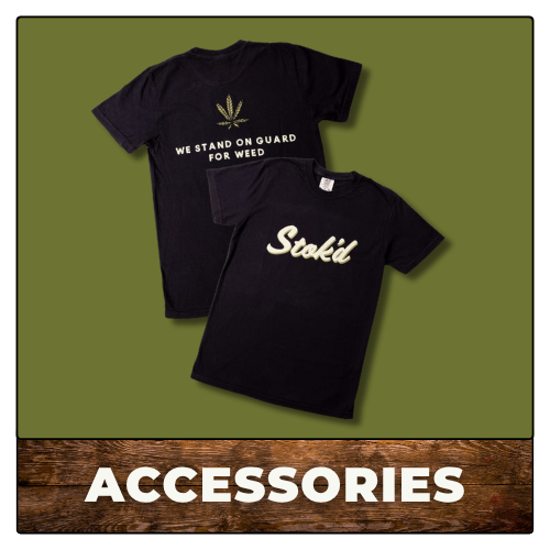Two black Stoki shirts on an olive background above a wooden “ACCESSORIES” banner