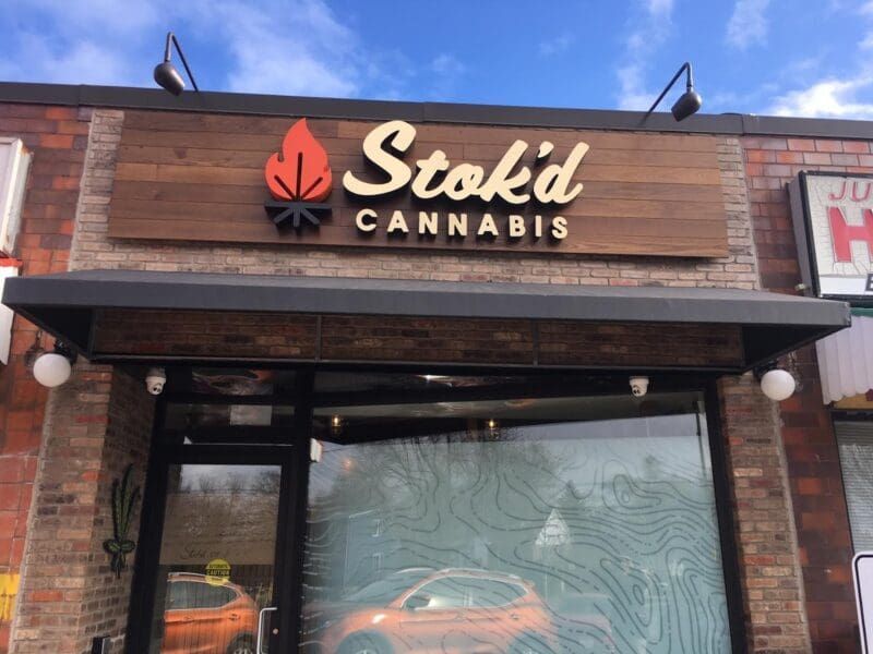 Storefront sign for Stokd Cannabis on a brick building with a wood facade and window display.