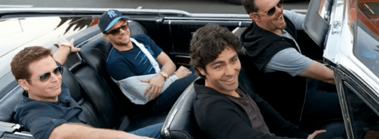 Four men riding in a convertible, smiling and wearing sunglasses in daylight