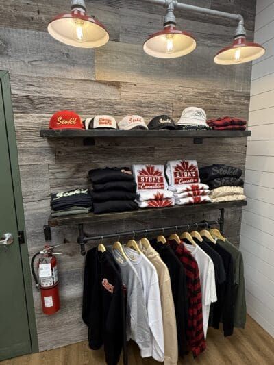 Clothing store display with shelves of folded shirts, hanging jackets, and three pendant lights on a gray wall