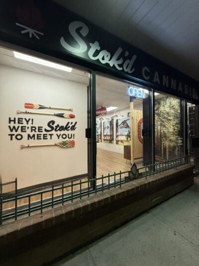 Stoki Cannabis storefront at night with a lit window sign reading “Hey, we’re Stoki to meet you.”