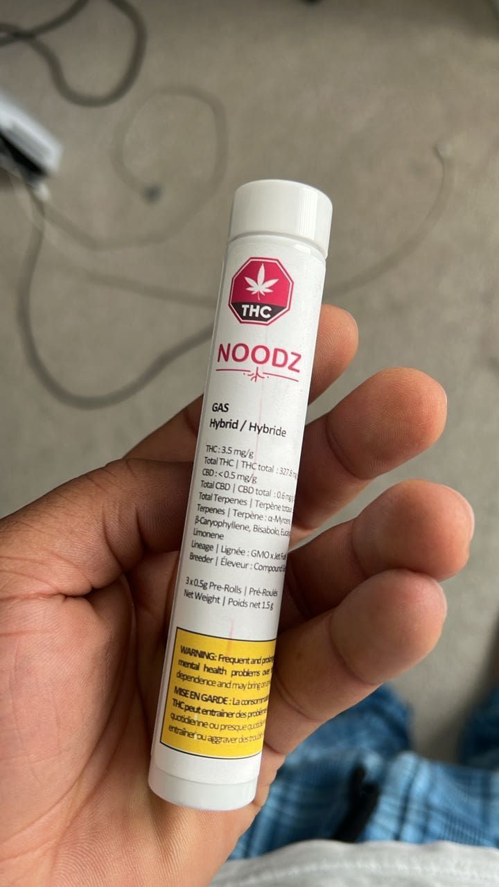 A hand holding a white cylindrical tube with a red logo and yellow warning label.