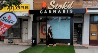 Storefront for Stoked Cannabis with black and orange sign, a person standing in front of the entrance.