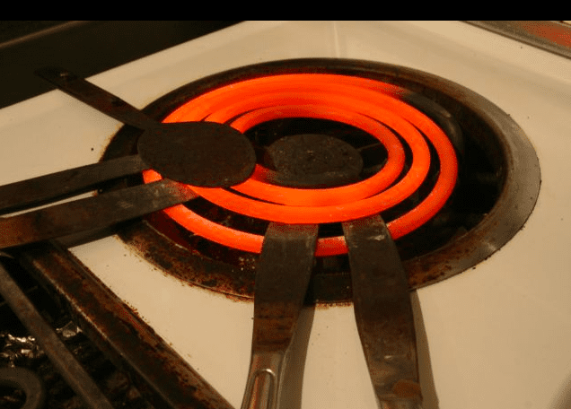 Glowing red electric stove burner with black tongs resting across it