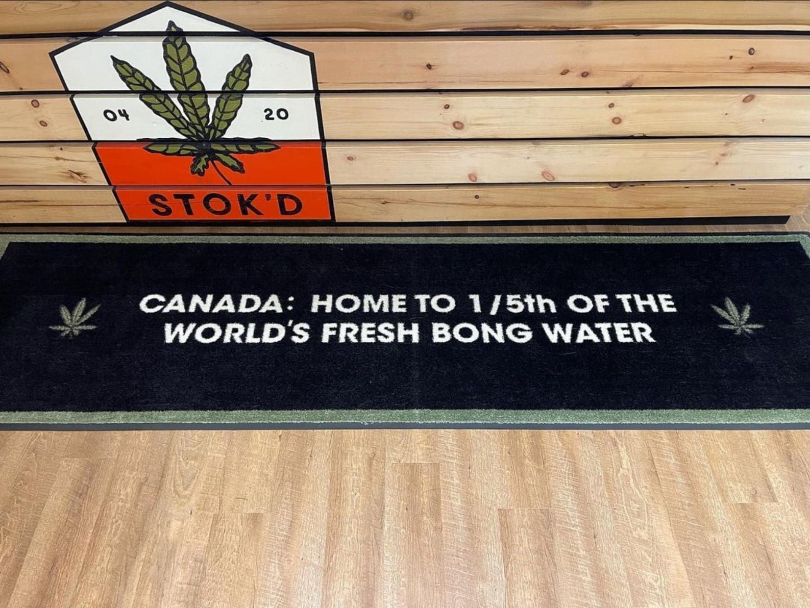 Wooden wall with cannabis leaf sign and black banner reading “Canada: Home to 1/5th of the world’s fresh bong water”