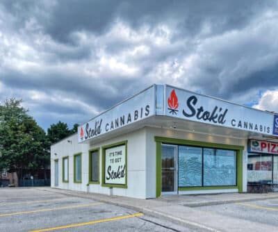 Stokd Cannabis storefront in a strip mall under cloudy skies, with large windows and parking lot