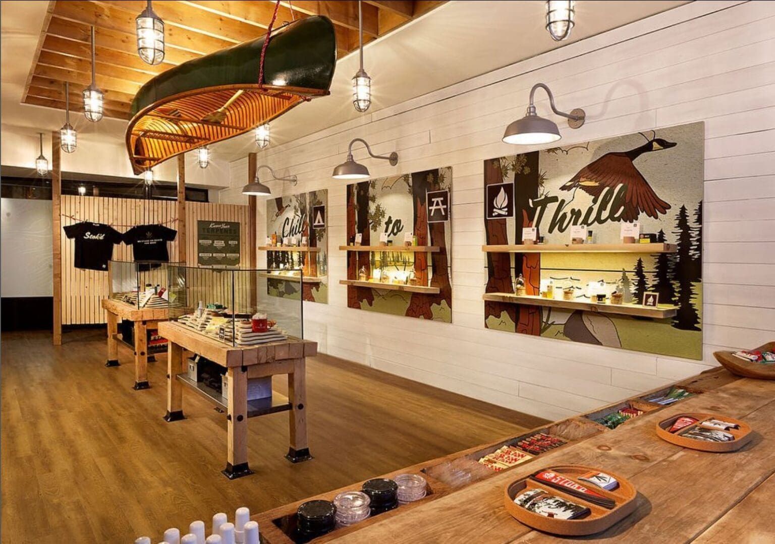 Interior of a surf shop with wooden floors, hanging lights, display tables, and wall art featuring surfboards.