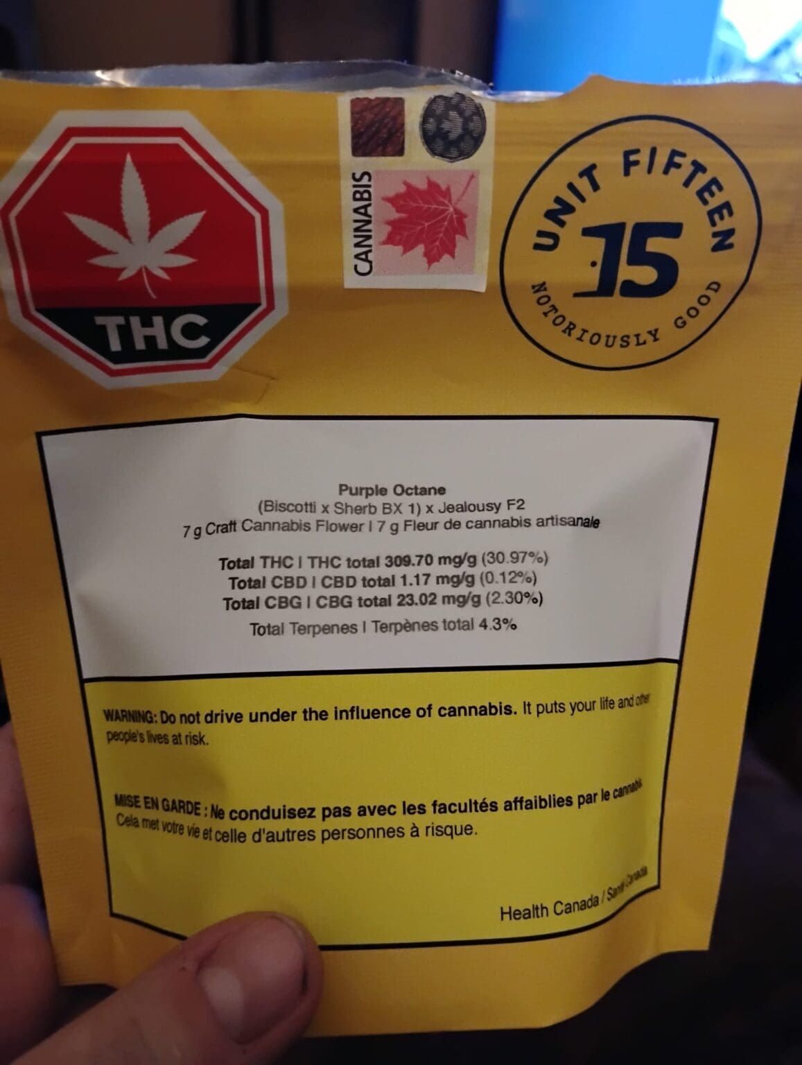 Hand holding a yellow THC cannabis package with red and black labels and a white product information sticker