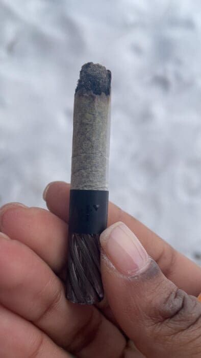 Hand holding a short black-and-gray cylindrical object against a snowy background