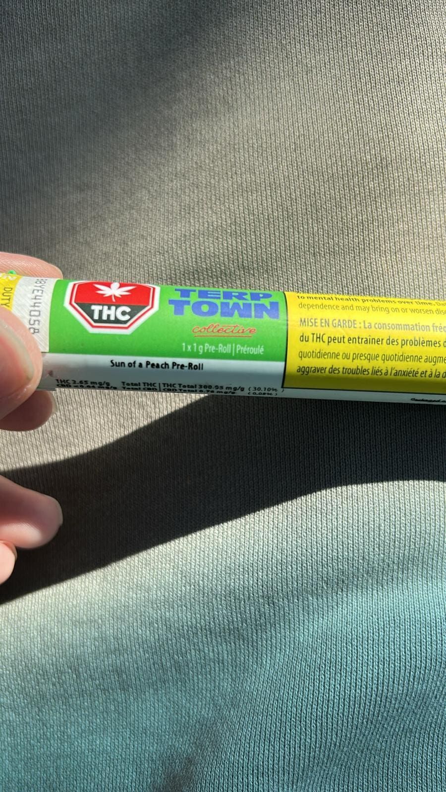 Hand holding a THC vape pen with a green-and-yellow label in sunlight on fabric.