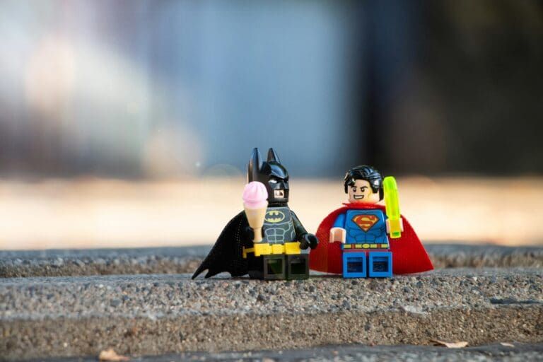 Batman and Superman LEGO figures standing side by side on a ledge, with the city blurred behind them