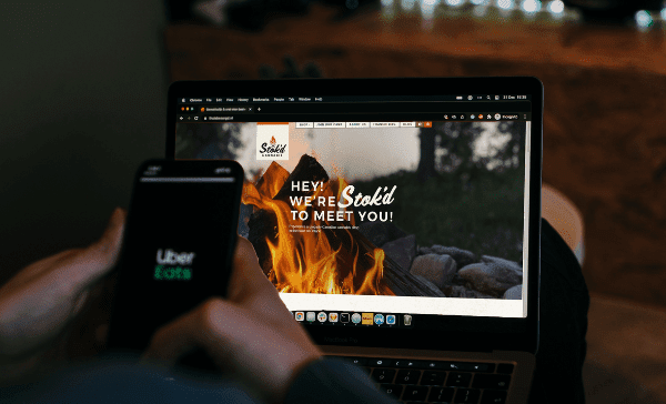 Hand holding a phone beside a laptop showing a website with “We’re still to meet you!” on the screen