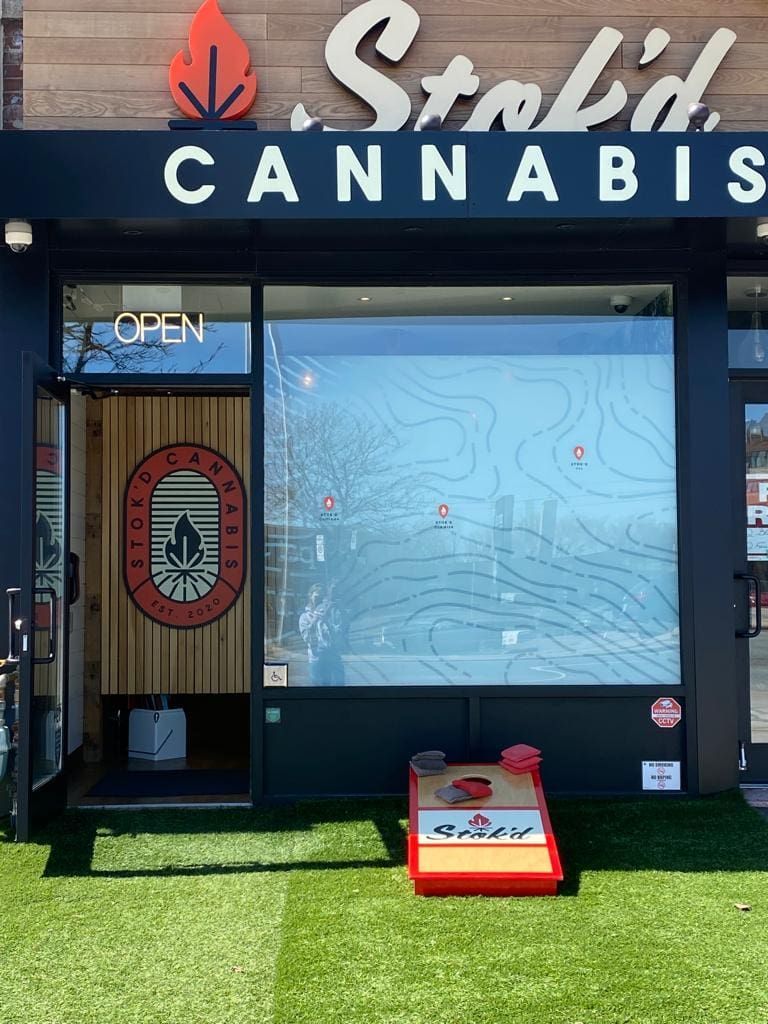 Storefront of Solid Cannabis with sign, glass door, window graphic, and small display sign on artificial grass.