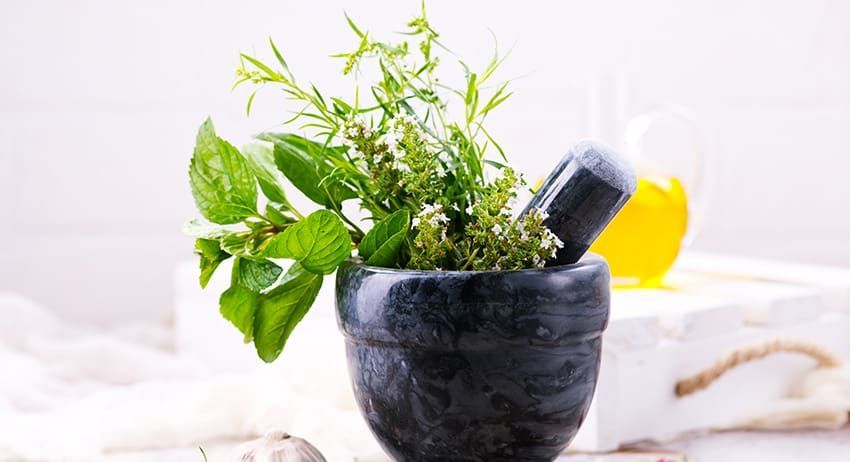 Fresh green herbs in a dark mortar with pestle on a light background
