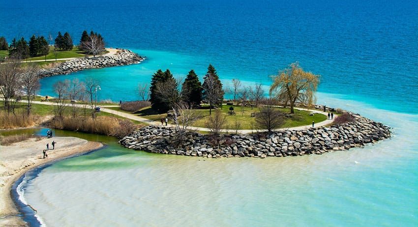 Small landscaped island with trees and stone shore in turquoise blue water, viewed from above