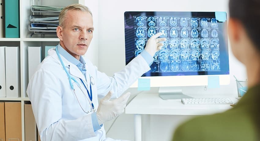 Doctor pointing at brain scans on a monitor in a bright clinic office