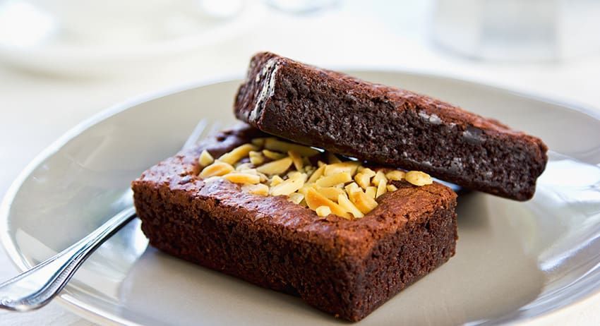 Two chocolate cake slices with shredded cheese on a white plate with a fork