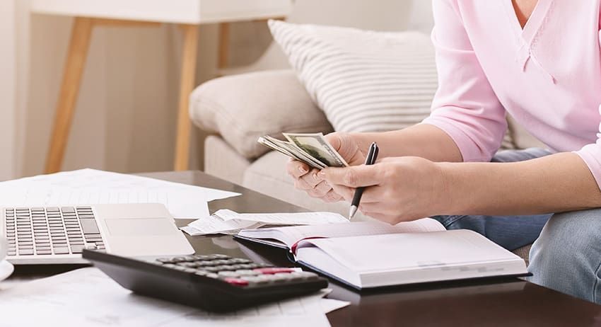 Person counting cash at a desk with a calculator and paperwork in a bright office setting