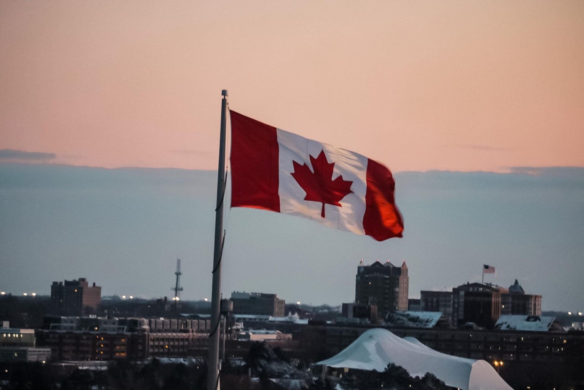 Canadian flag waving over a city skyline at dusk