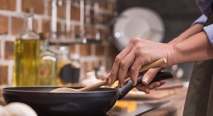 Hands stirring food in a black pan on a stovetop in a kitchen