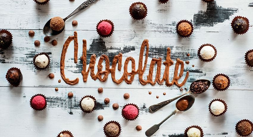 Chocolate lettering surrounded by assorted chocolates and truffles on a white wooden background