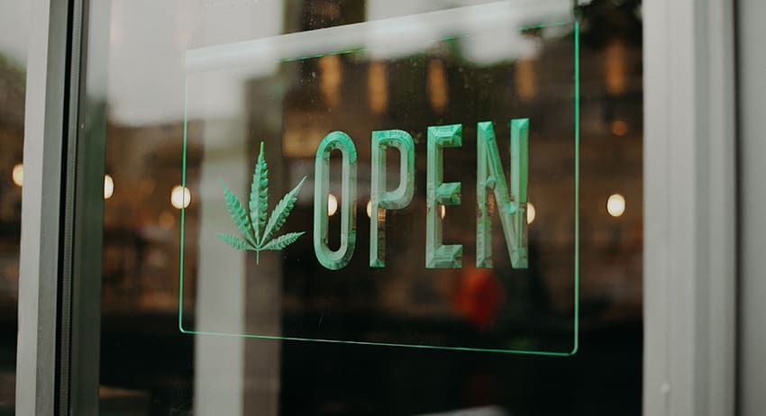 Green “OPEN” sign in a shop window with a cannabis leaf icon.