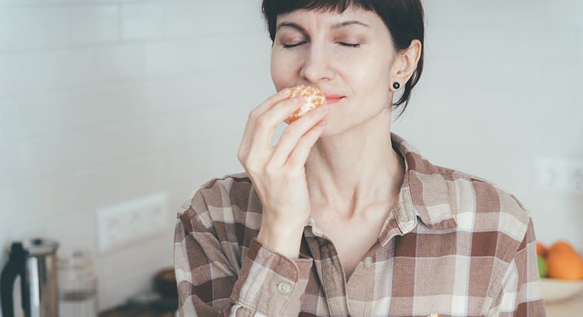 Person eating a slice of pizza in a bright kitchen, eyes closed in enjoyment