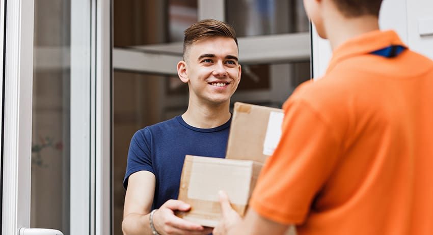 Smiling person handing a cardboard package to someone in an orange shirt at a doorway