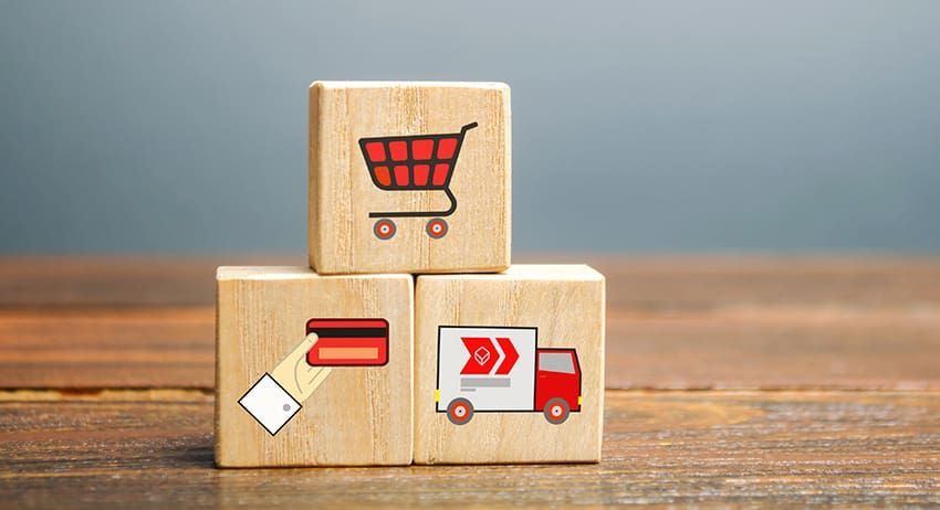 Wooden blocks with shopping cart, delivery truck, and package icons on a tabletop