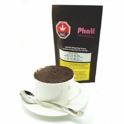 Cup of ground coffee beside a black Phat pack with a silver spoon on a white surface