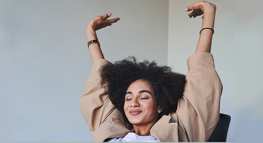 Woman smiling with arms raised against a plain light wall