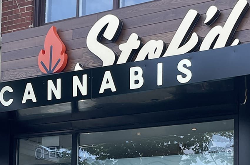 Storefront sign for “Stak’d Cannabis” with white lettering and a red leaf logo above the entrance