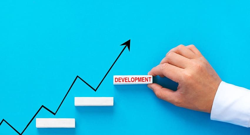 Hand placing “development” label on upward growth chart with steps and arrow on blue background