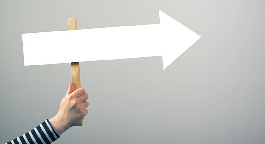 Hand holding a white right-pointing arrow sign against a gray background