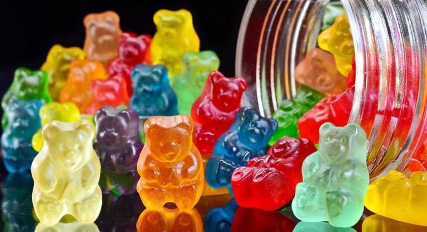 Colorful gummy bears spilling from a jar on a black background