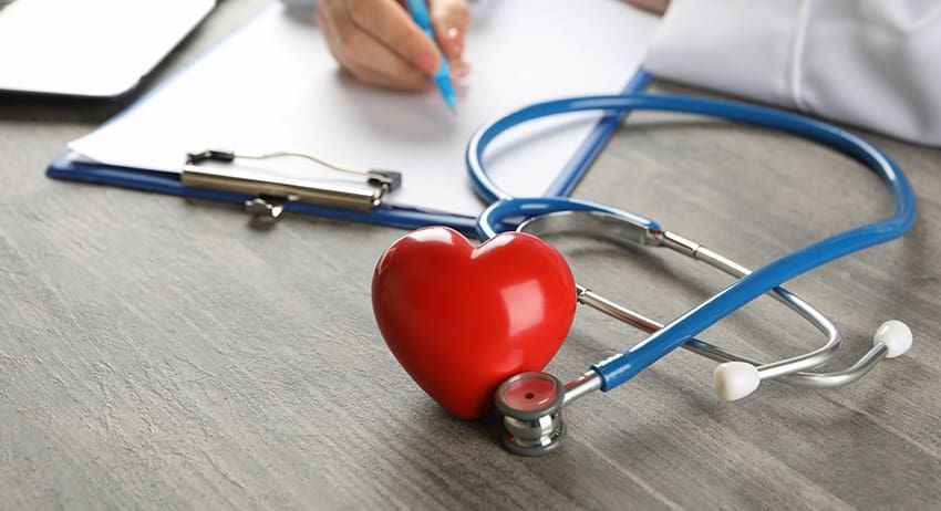 Red heart-shaped toy with a stethoscope on a doctor's clipboard in a medical setting