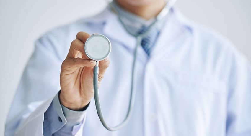 Doctor holding a stethoscope in a white coat against a blurred clinical background